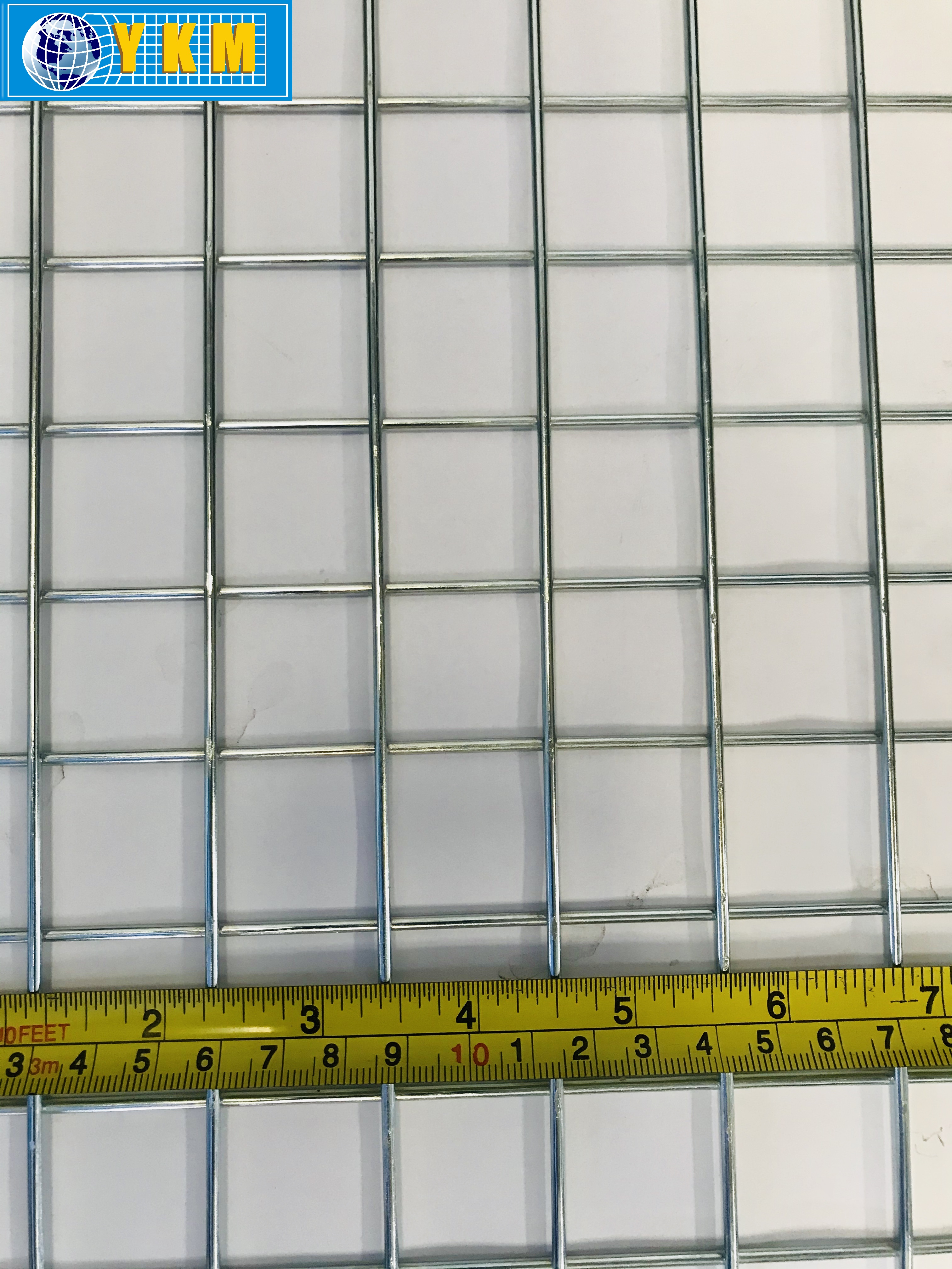 Close-up photograph of a welded square wire grid beside a measuring tape